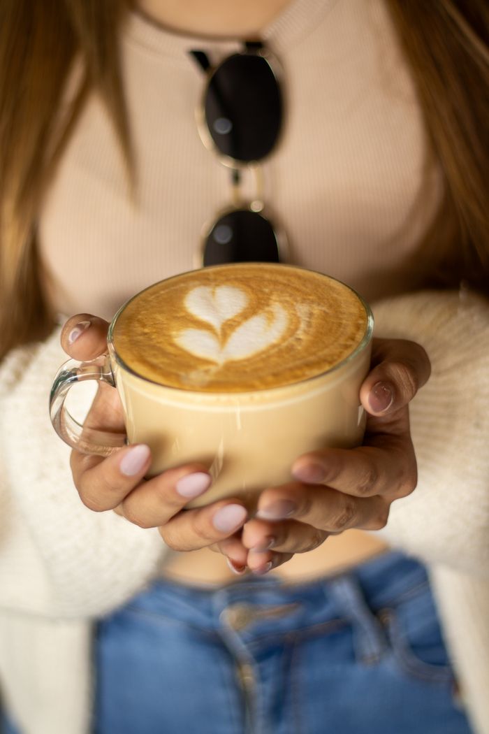 Close-up of a woman holding a latte with heart-shaped art in a trendy cafe setting.